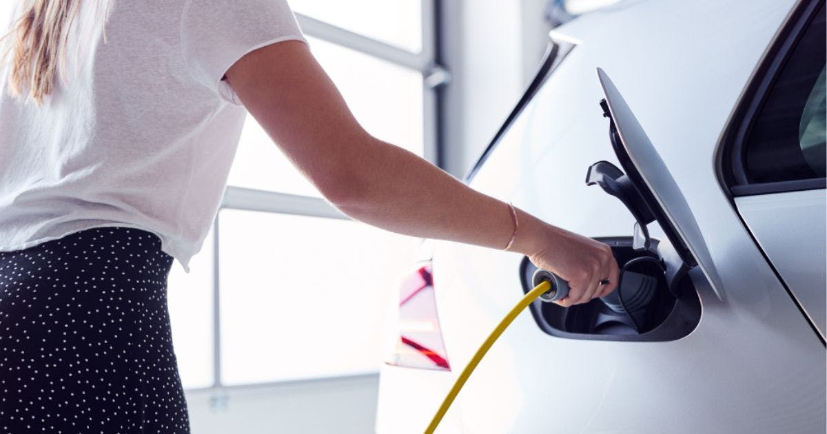 Woman plugging in EV charger to white EV in garage
