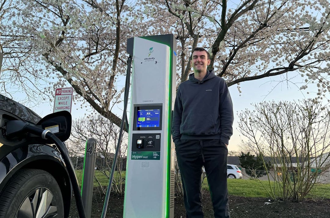 Man standing next to a fast EV charger with black Nissan Ariya charging 