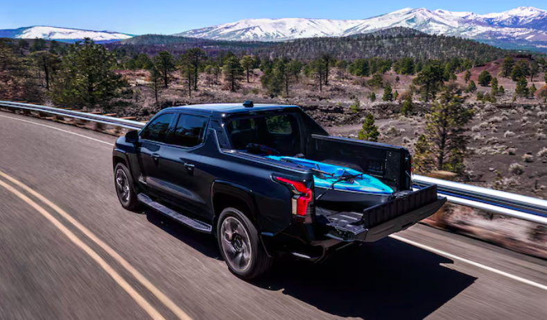 Chevrolet Silverado EV truck driving on highway with snowy mountains in background